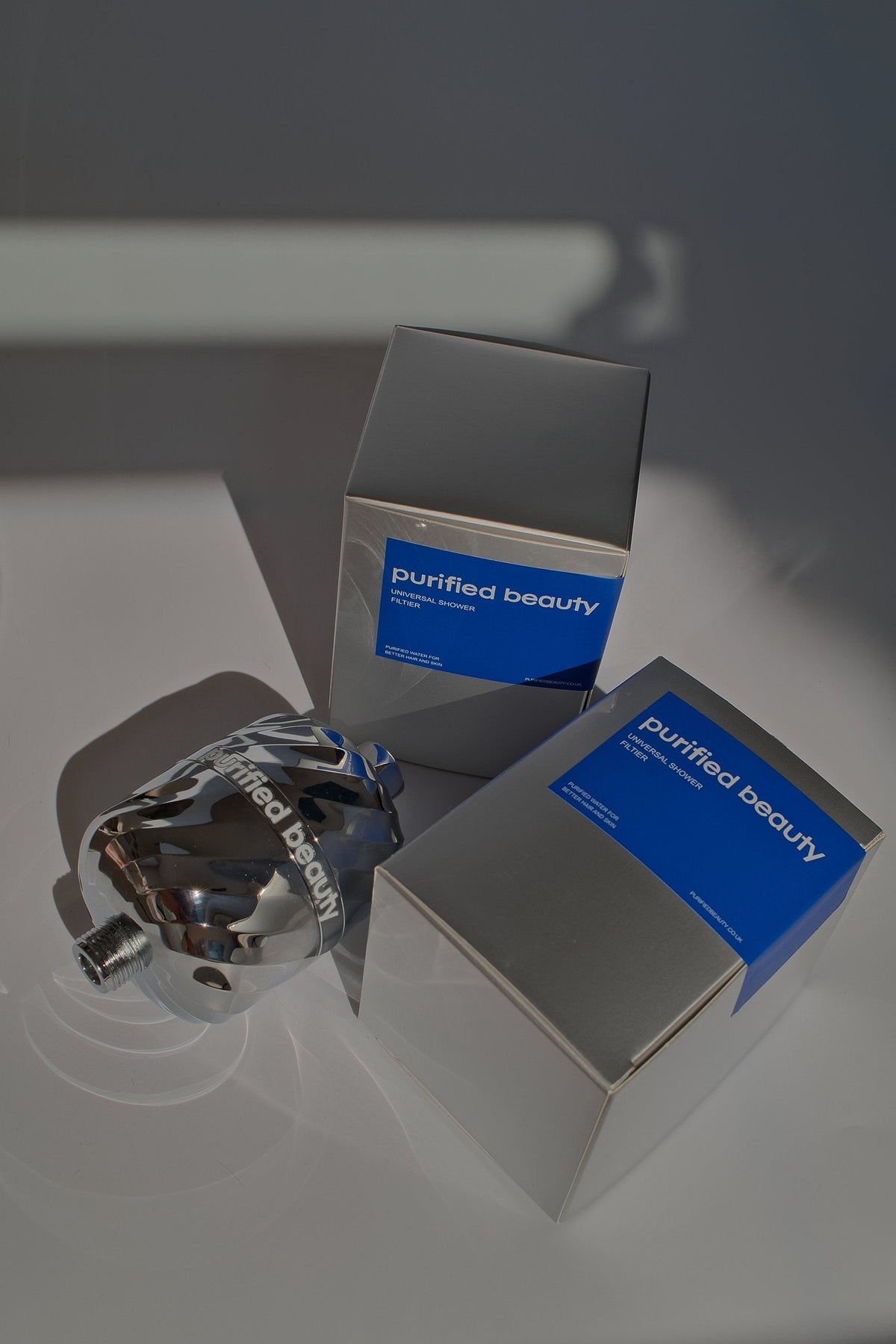 Purified Beauty chrome shower filter leaning on packaging